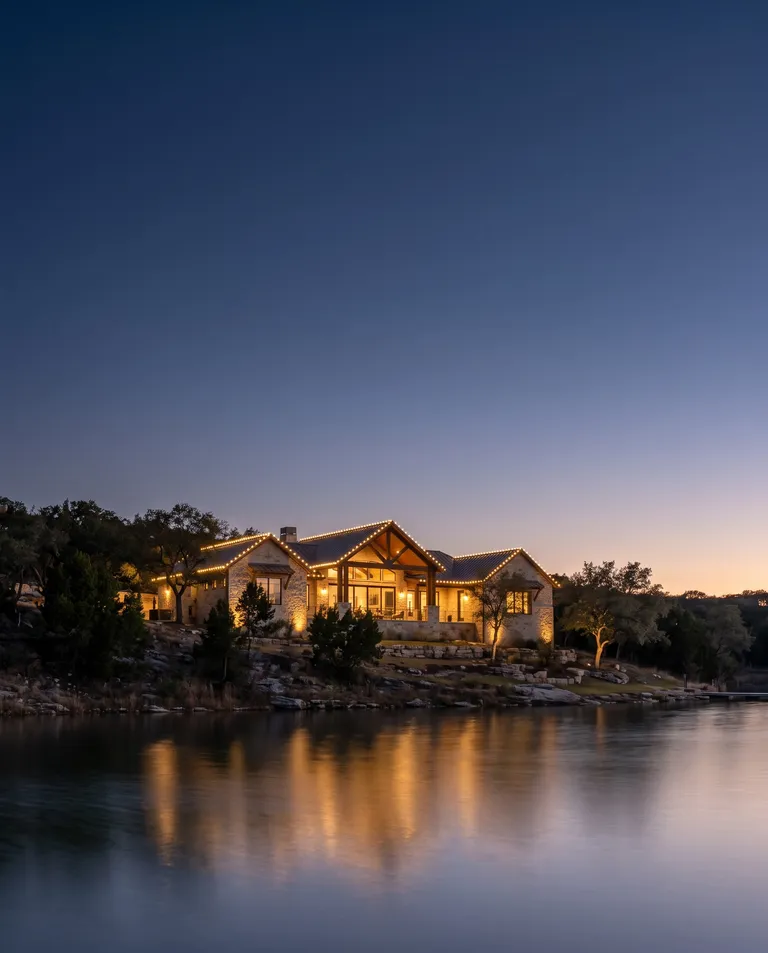 Lake house on a hillside above still water at blue hour with a warm white lit roofline reflecting on Canyon Lake