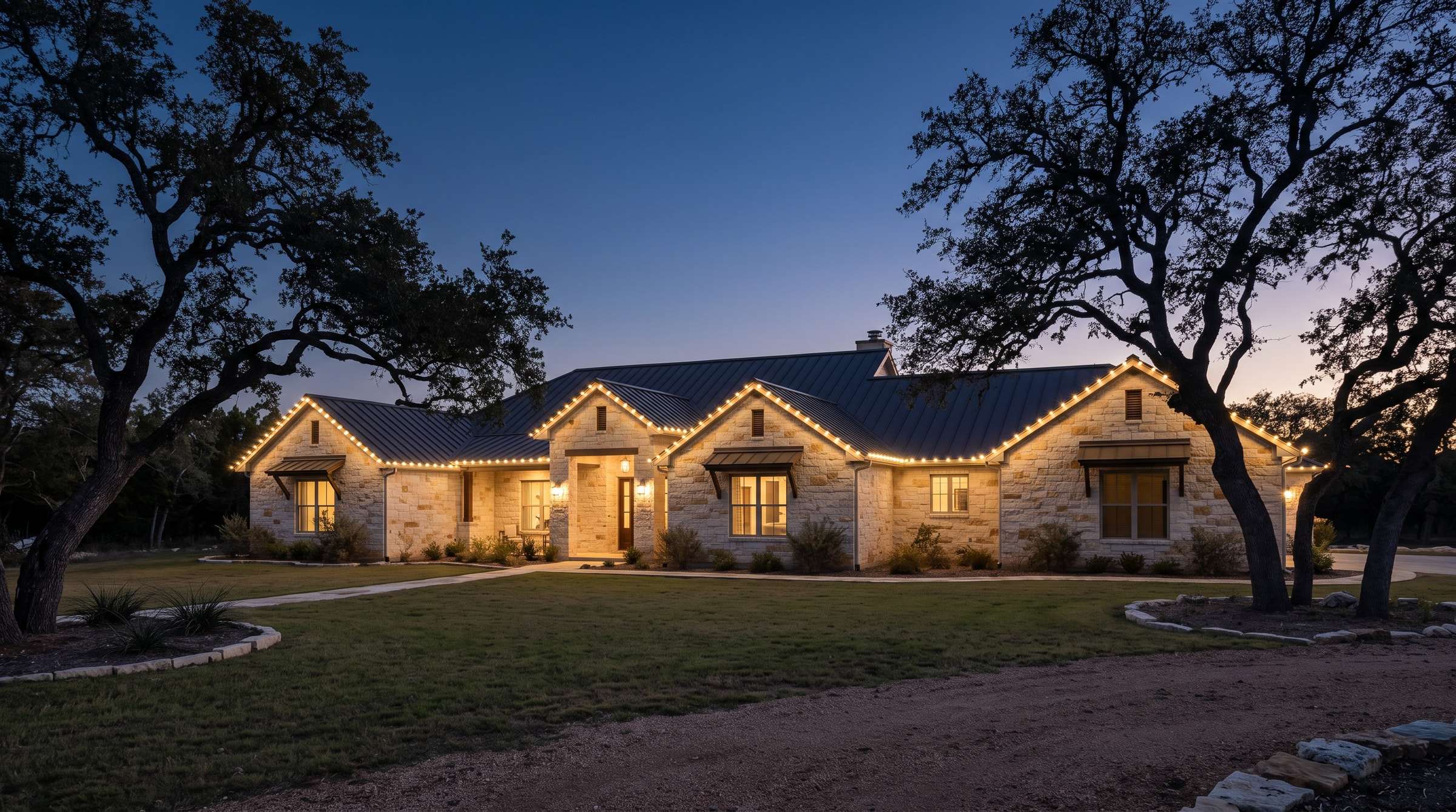 Single-story limestone ranch home with a metal roof outlined in warm white C9 bulbs at blue hour